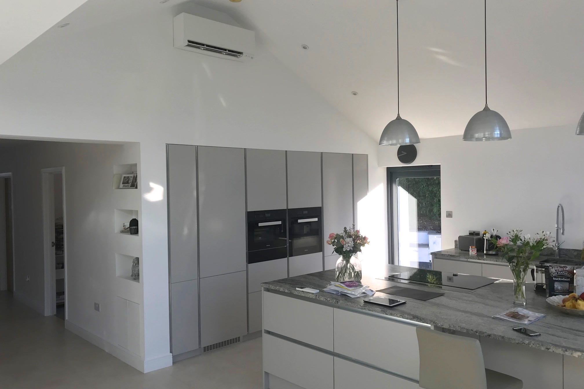 White wall mounted domestic air conditioning unit in open plan kitchen over fridge an oven units side view