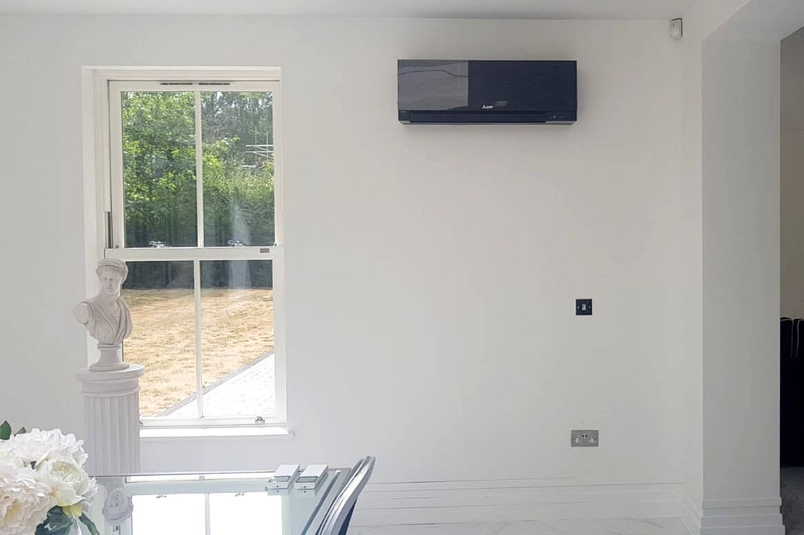 Black mitsubishi electric wall mounted air conditioning unit in living space by dining table and window fitted by SubCoolFM