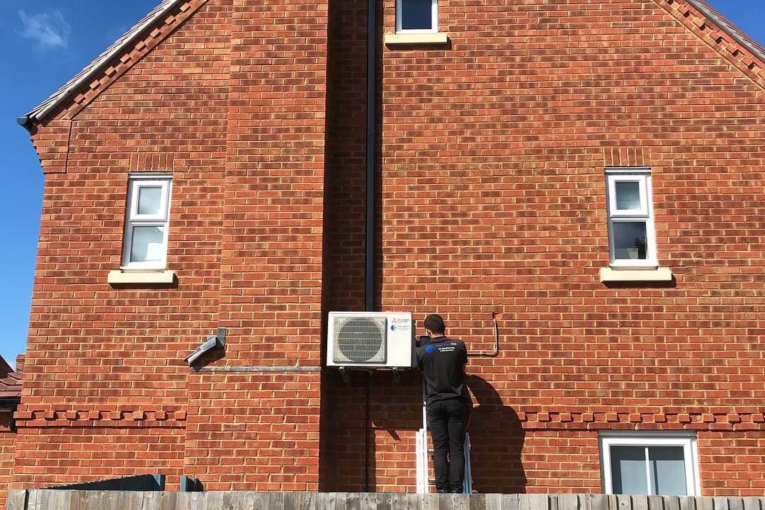 Exterior wall mounted mitsubishi electric domestic air conditioning unit neatly fitted by SubCool FM with engineer up ladder undertaking maintenance