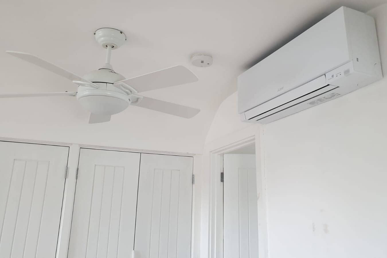 White wall mounted mitsubishi electric zen air conditioning unit in white room next to ceiling fan and cupboards
