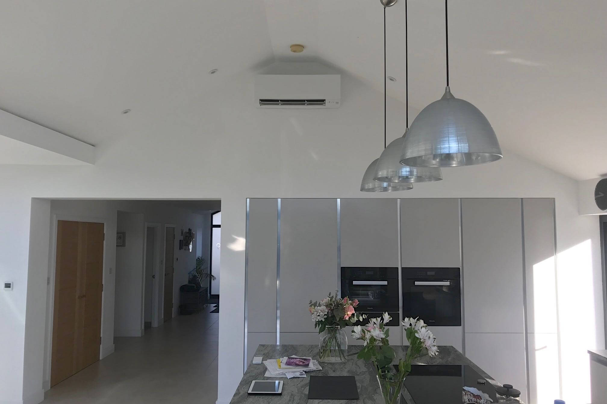 White wall mounted domestic air conditioning unit in open plan kitchen over fridge an oven units