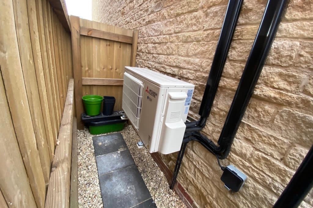 Mitsubishi Electirc external unit on side of house by path to garden with black piping
