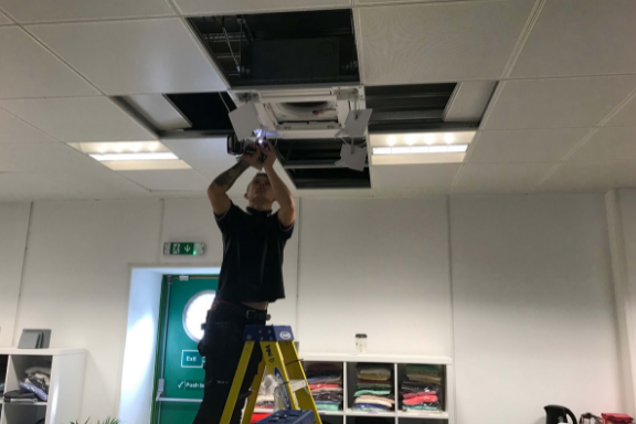Air conditioning engineer fixing in ceiling cassette in retail outlet